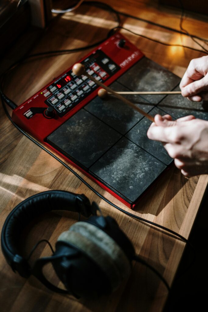 Close-up of hands playing an electronic percussion pad with drumsticks in a home studio.